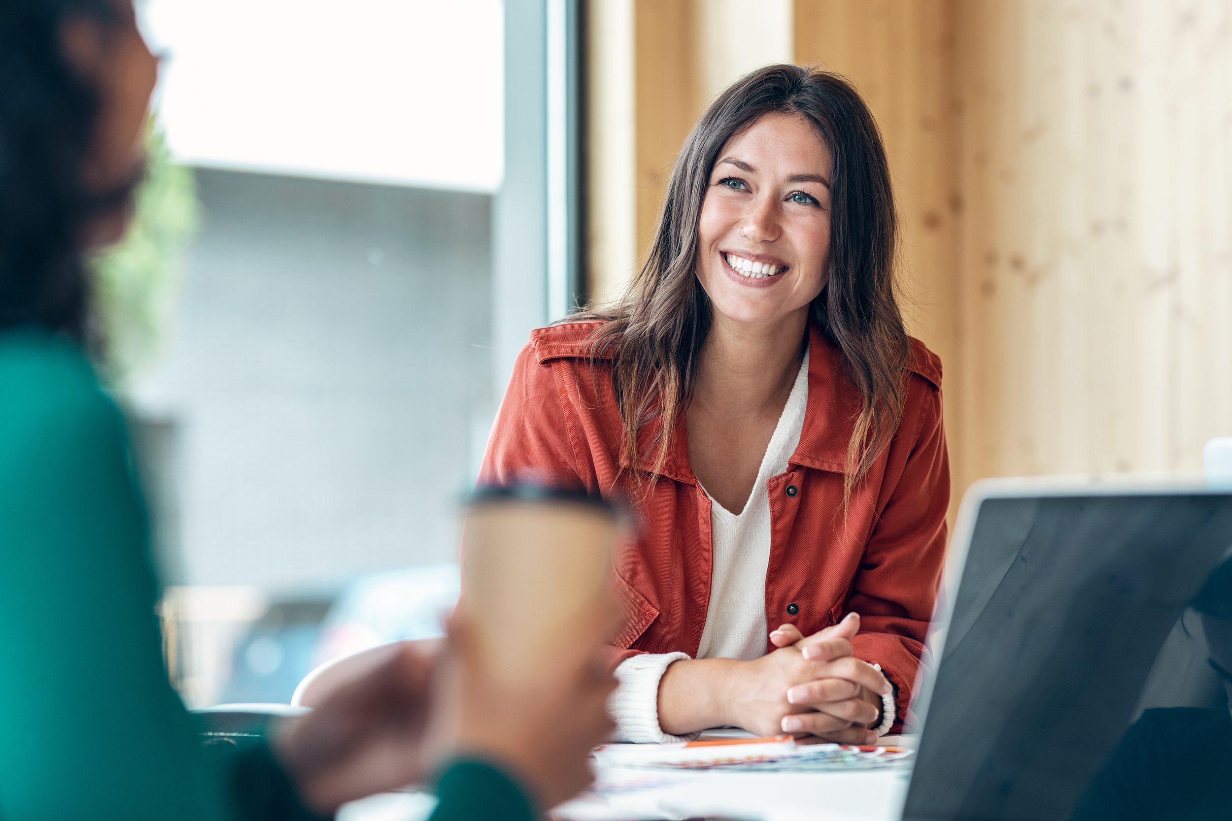 Shot of smiling young business woman listening her partner on coworking space.