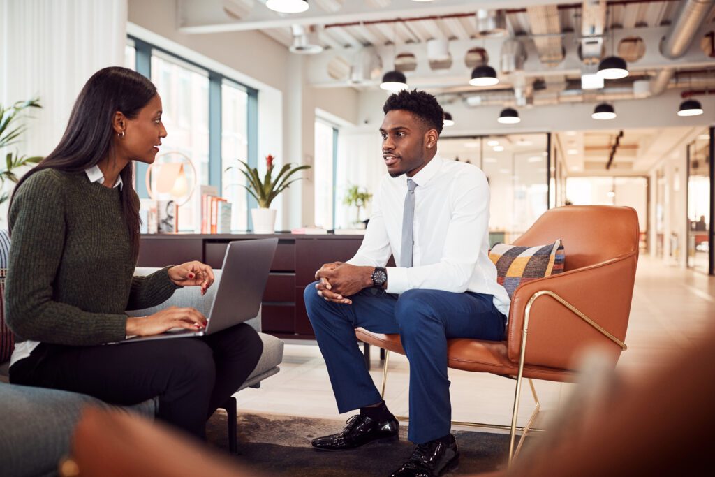 Businesswoman Reviewing Job Performance of Male Employee In Seating Area Of Modern Office Businesswoman Reviewing Job Performance of Male Employee In Seating Area Of Modern Office