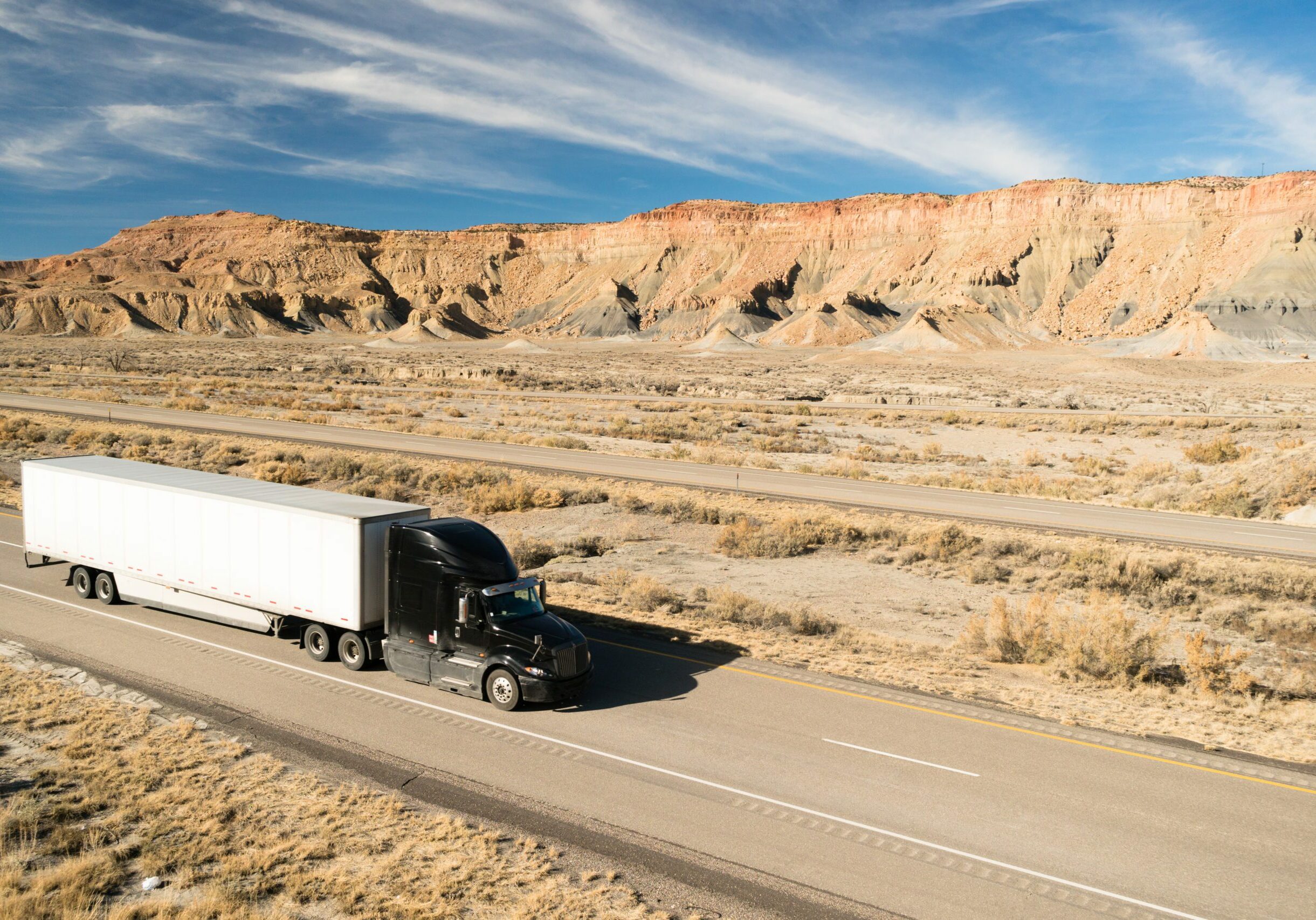 A black big rig rolls across Utah on a devided highway