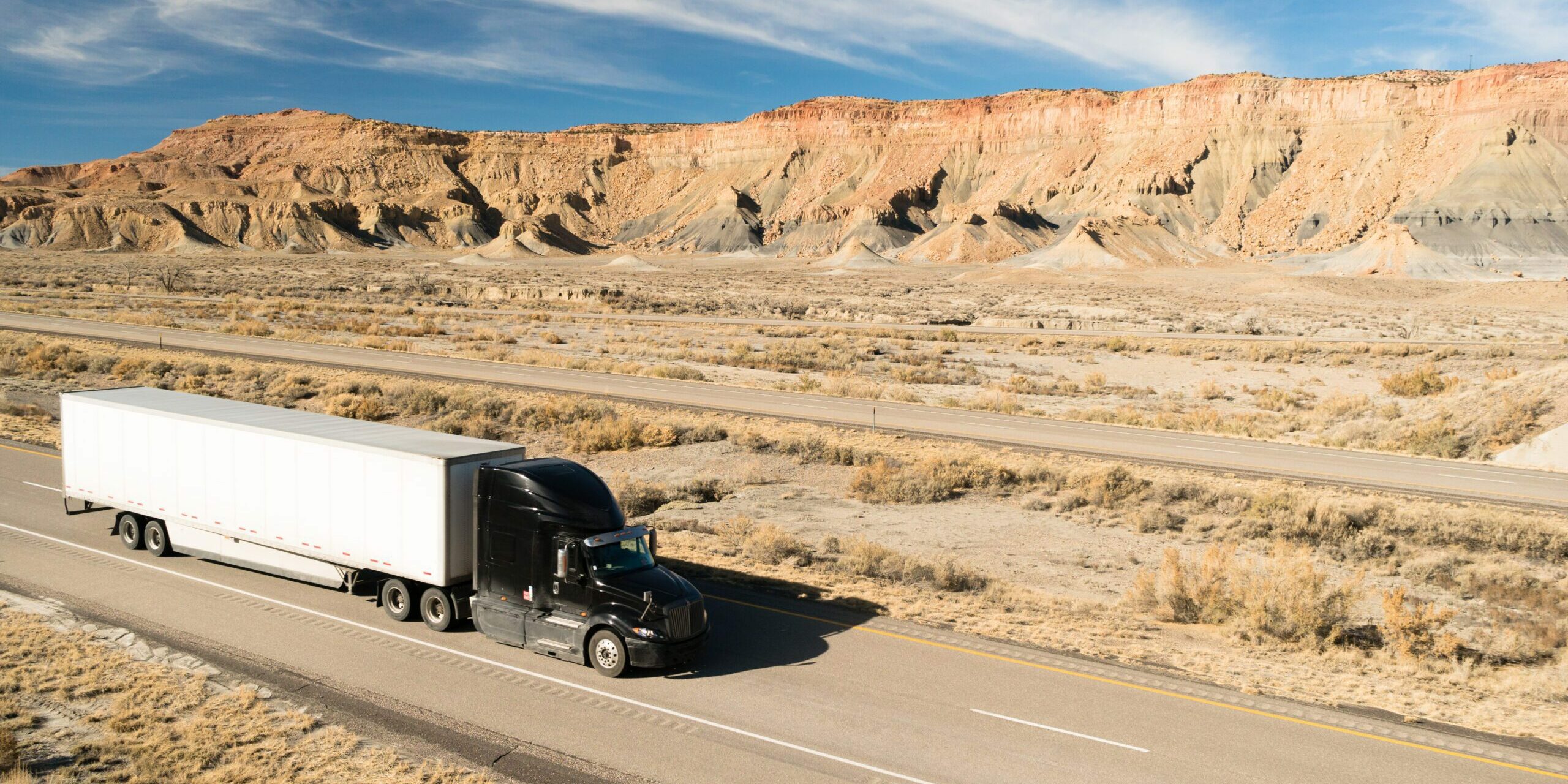 A black big rig rolls across Utah on a devided highway