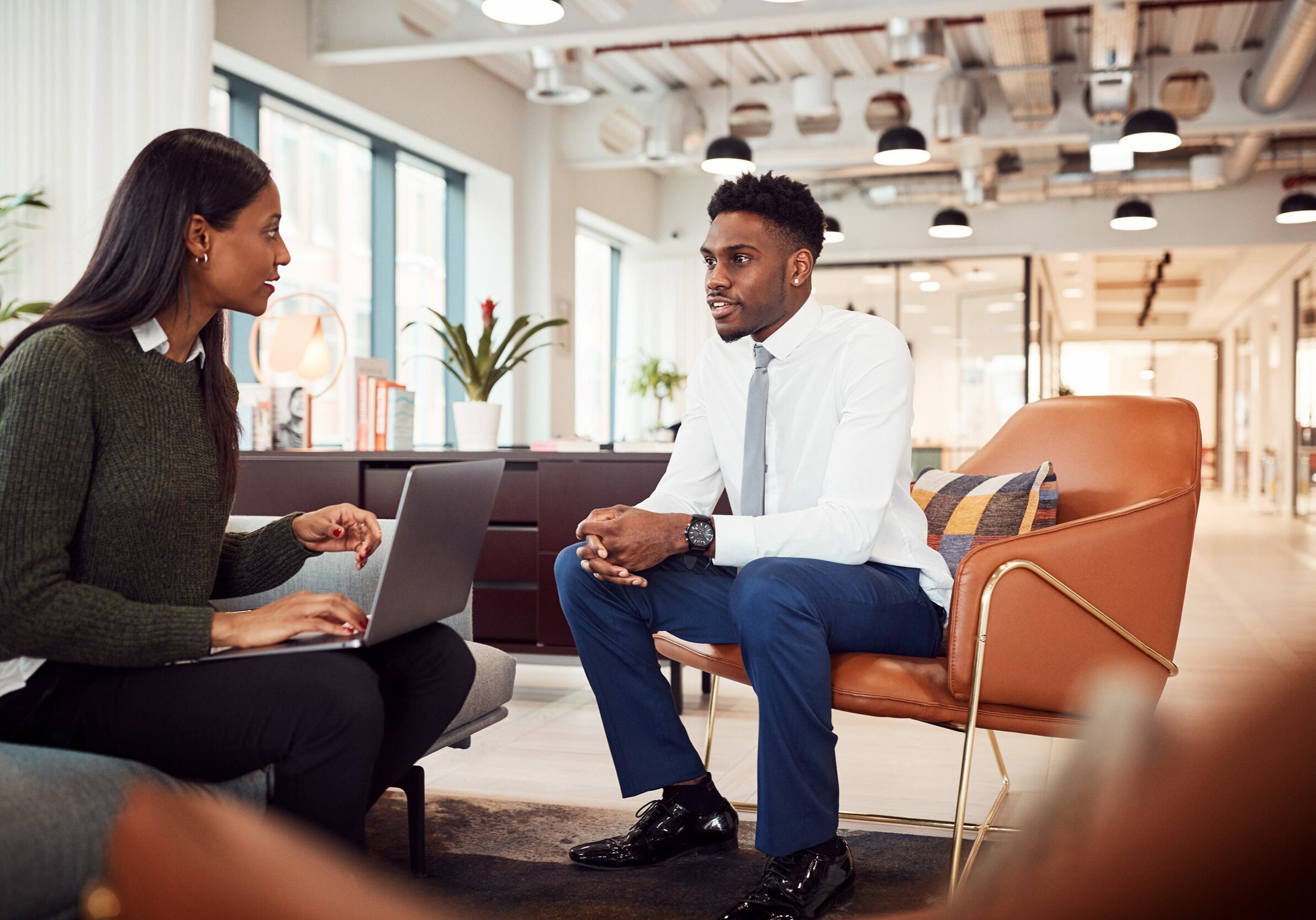 Businesswoman Reviewing Job Performance of Male Employee In Seating Area Of Modern Office